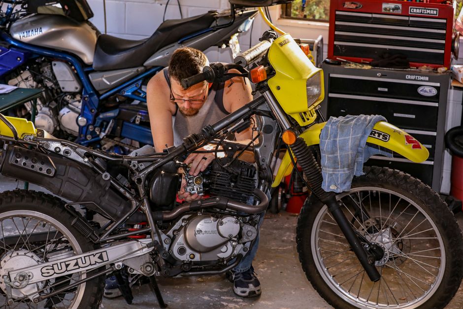 A mechanic repairs a Suzuki motorcycle engine inside a well-equipped garage.